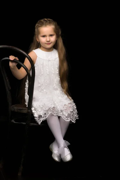 Portret van een klein meisje zittend op een oude Weense stoel, zwarte achtergrond. — Stockfoto