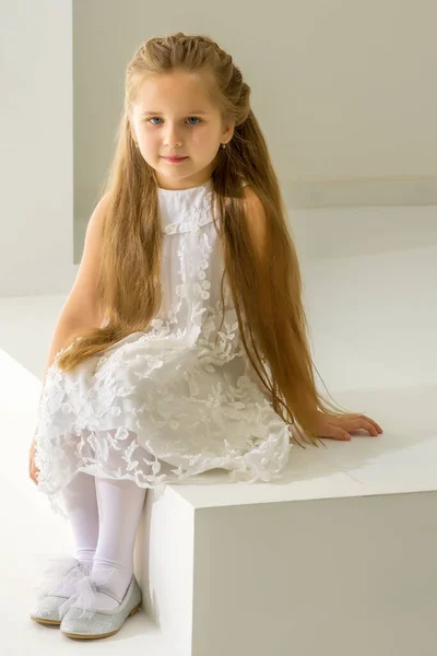 Linda niña está sentada en el estudio en las escaleras blancas. estilo y concepto de moda, infancia feliz. —  Fotos de Stock