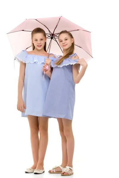 Zwei hübsche Schwestern in identischen hellen Kleidern, die unter Umb stehen — Stockfoto