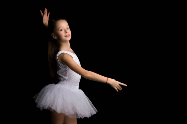 Schattig klein meisje in een tutu en pointe schoenen is dansen in de studio op een zwarte achtergrond. — Stockfoto