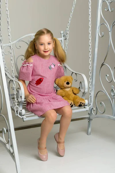 Маленькая девочка качается на качелях с плюшевым мишкой. — стоковое фото