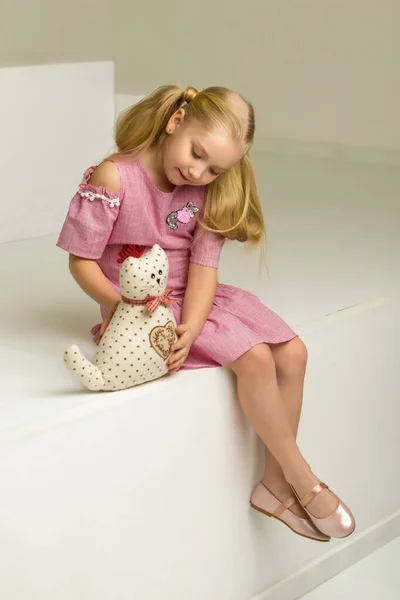 Linda niña está sentada en el estudio en las escaleras blancas. estilo y concepto de moda, infancia feliz. — Foto de Stock