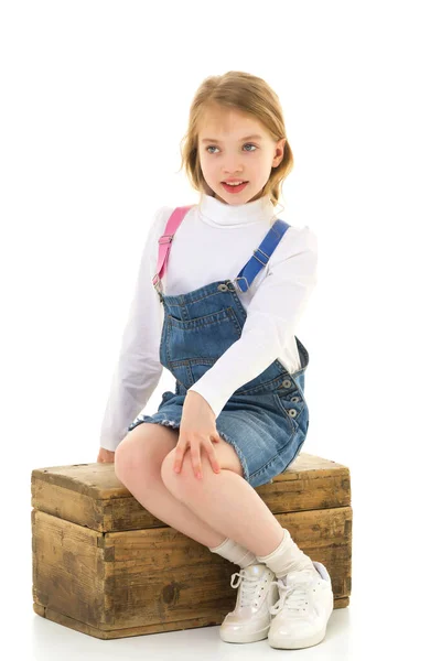 Ein kleines Mädchen sitzt auf einer Holzkiste. — Stockfoto
