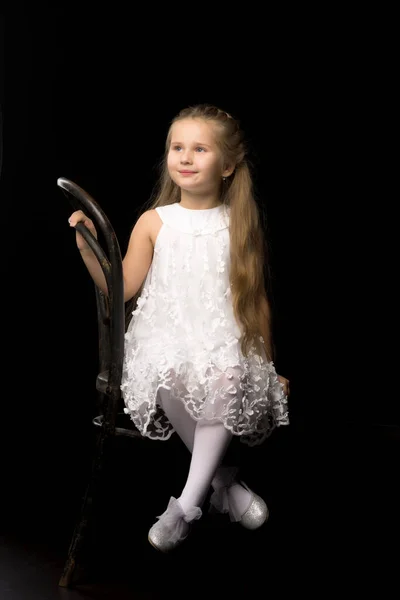 Retrato de uma menina sentada em uma velha cadeira vienense, fundo preto. — Fotografia de Stock