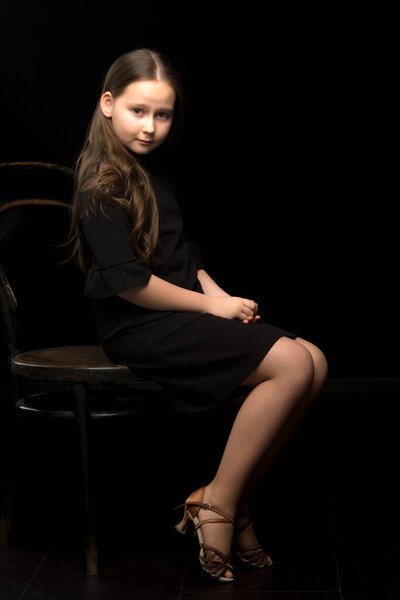 Portrait of a little girl sitting on an old Viennese chair, black background.
