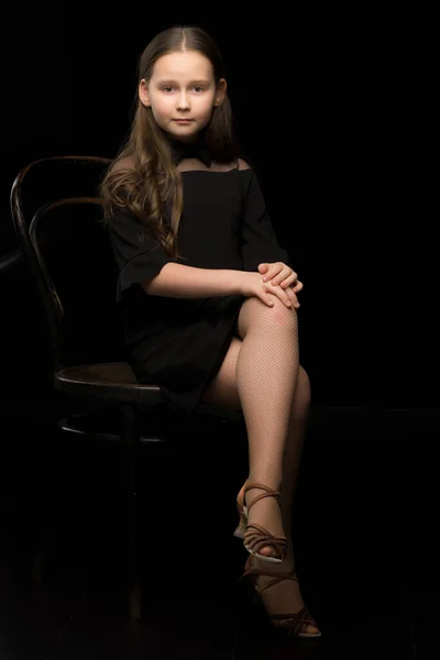 小さな女の子の肖像画古いウィーンの椅子に座って、黒の背景. — ストック写真