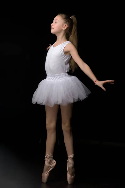 Aranyos kislány egy tütü és pointe cipő táncol a stúdióban egy fekete háttér. — Stock Fotó