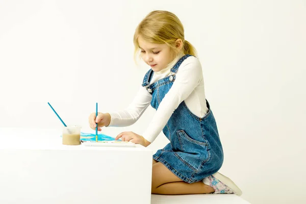 Cute Blonde Girl Sitting on Her Knees and Painting with Brush.