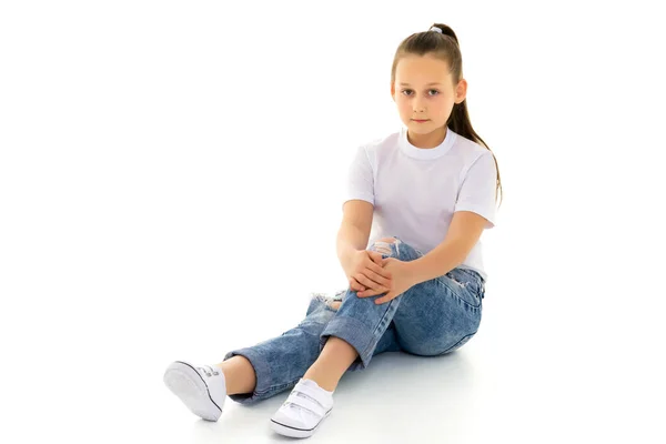 Ein kleines Mädchen sitzt in einem weißen T-Shirt auf dem Boden. — Stockfoto