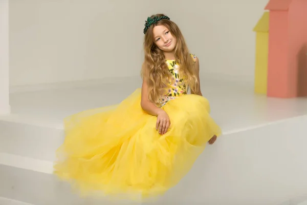 Słodka dziewczynka siedzi w studio na białych schodach. styl i koncepcja mody, szczęśliwe dzieciństwo. — Zdjęcie stockowe
