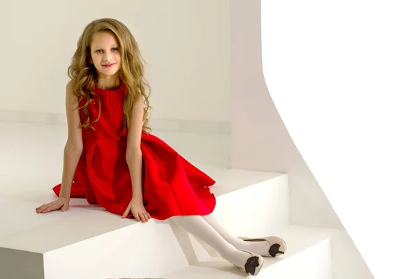 Menina bonita vestindo vestido vermelho agradável sentado em escadas brancas — Fotografia de Stock