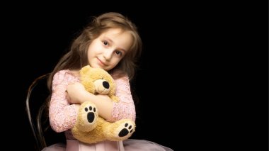 Siyah arka planda oyuncak ayısı olan küçük bir kız..