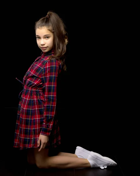 Una niña está arrodillada sobre un fondo negro en el estudio. —  Fotos de Stock