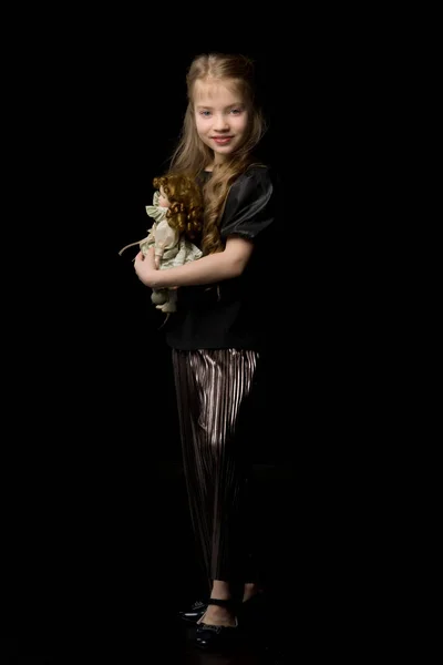 Ein kleines Mädchen spielt mit einer Puppe auf schwarzem Hintergrund. — Stockfoto