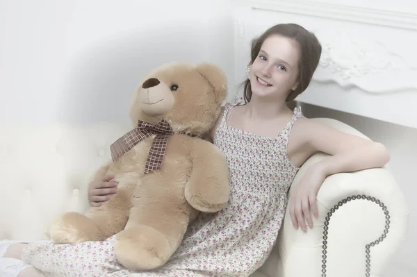 Schöne Teenager-Mädchen im Schulalter sitzen auf einem Sofa mit einem Teddybär. — Stockfoto