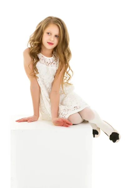 Menina loira bonita em vestido branco sentado no cubo em seu joelho — Fotografia de Stock