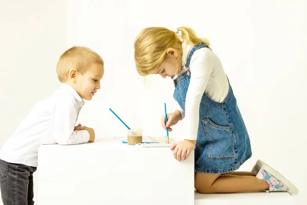 Cute Girl Sitting on Her Knees and Painting, Brother Looking at Her. — Stock Photo, Image