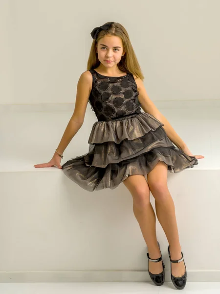 Niña con estilo en un vestido se sienta en un parapeto blanco. Estudio fotografía. — Foto de Stock