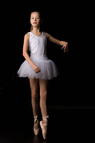 Menina bonito em um tutu e sapatos pontiagudos está dançando no estúdio em um fundo preto. — Fotografia de Stock