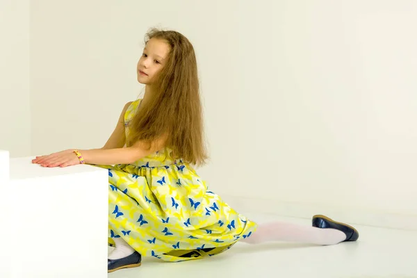 Mooi meisje in een gele jurk en blauwe schoenen zit op een touw. — Stockfoto