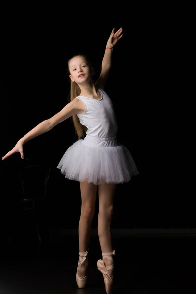 Menina bonito em um tutu e sapatos pontiagudos está dançando no estúdio em um fundo preto. — Fotografia de Stock