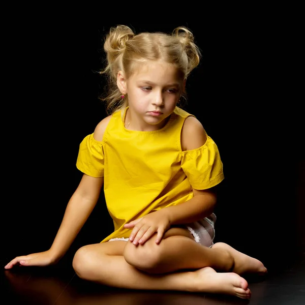 Little girl is sitting on the floor.The concept of a happy childhood.Isolated over black background. — Stock Photo, Image