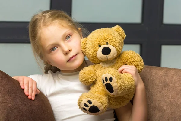 Little girl on sofa hugging teddy bear. — Stock Photo, Image