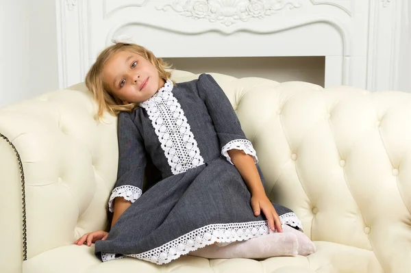 Klein meisje zit op de bank. Het concept van een gelukkige jeugd.. — Stockfoto