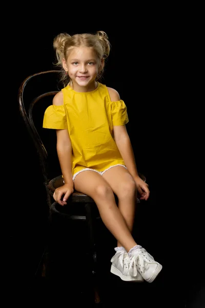 Retrato de uma menina sentada em uma velha cadeira vienense, fundo preto. — Fotografia de Stock