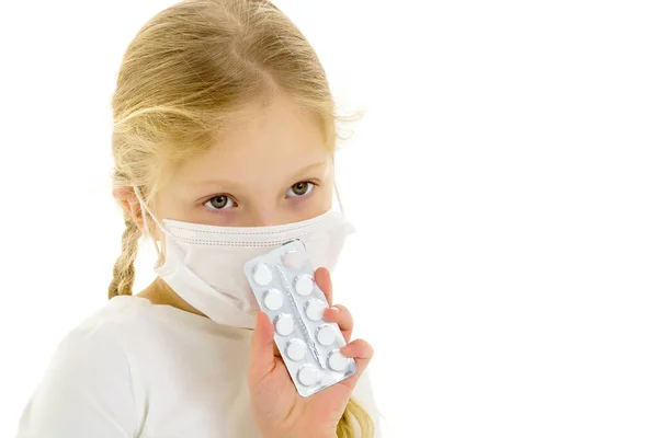 Little girl in a medical mask.She holds a pack of pills in her hand. Disease concept, covid-19. — Stock Photo, Image