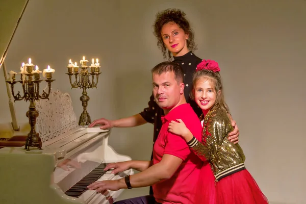 Família na véspera de Natal perto de um velho piano branco no qual velas — Fotografia de Stock