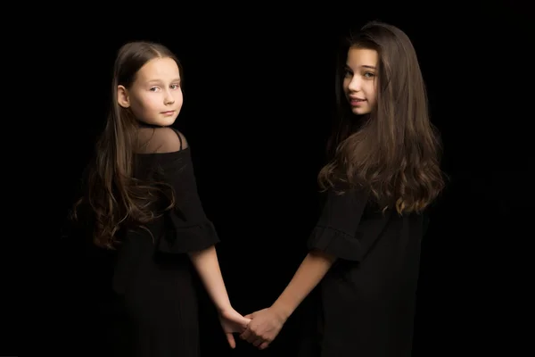 Дві маленькі дівчата тримаються за руки, на чорному тлі . — стокове фото