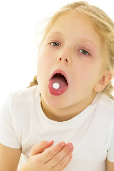 Uma menina em uma camiseta branca limpa engole uma pílula, a pílula fica em sua língua. Conceito de Covid-19, vírus, doença, tratamento. — Fotografia de Stock