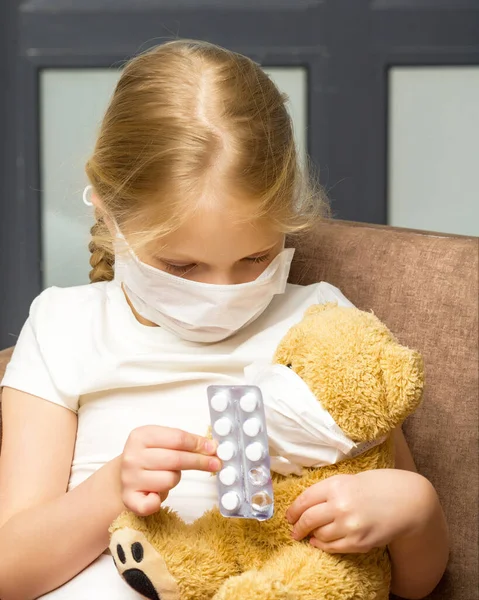 Little girl in a medical mask hugs a teddy bear. covid concept. — Stock Photo, Image