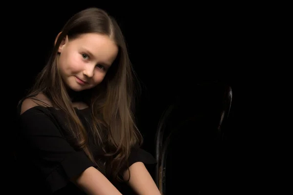 Πορτρέτο ενός μικρού κοριτσιού που κάθεται σε μια παλιά Βιεννέζικη καρέκλα, μαύρο φόντο. — Φωτογραφία Αρχείου