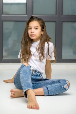 Küçük kız büyük bir panoramik pencerenin yanında poz veriyor.