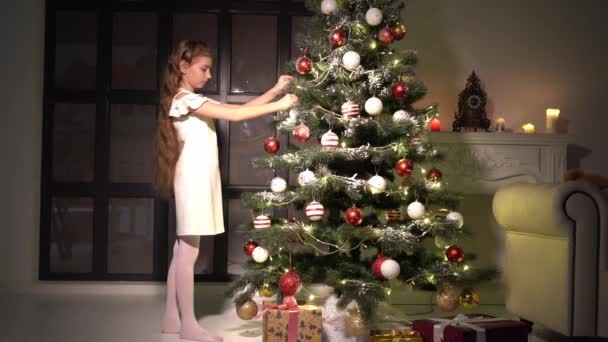 Маленька дівчинка прикрашає ялинку. Новорічна концепція, сімейні свята . — стокове відео