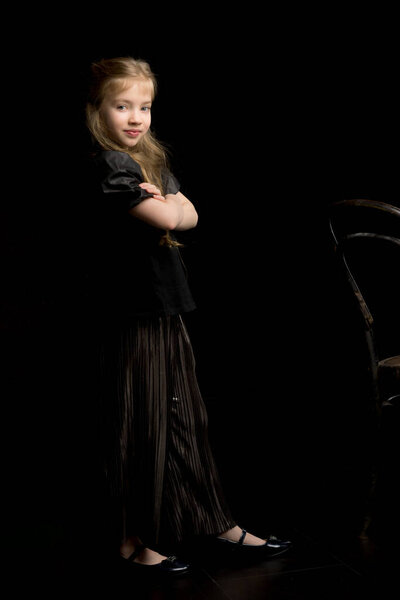 Portrait of a girl standing on a black background near the old Viennese chair.