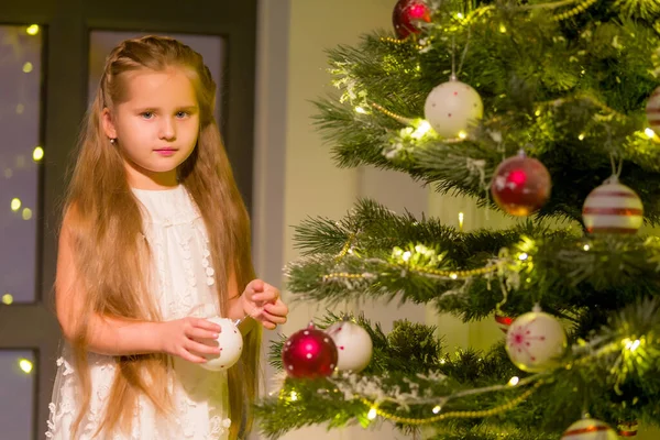 Meisje in stijlvolle jurk zitten op de vloer in de voorkant van de kerstboom. — Stockfoto
