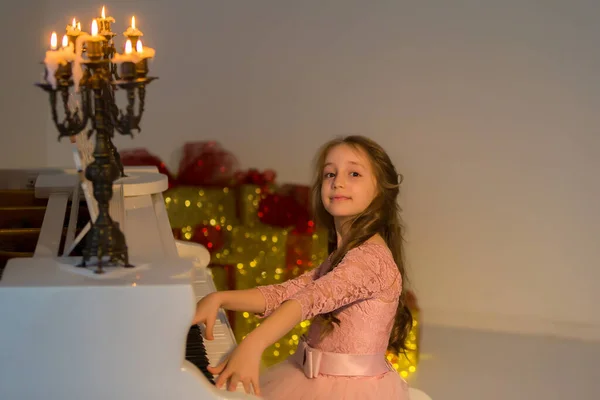 Chica posando mientras está sentado en el piano decorado con velas que se queman. —  Fotos de Stock
