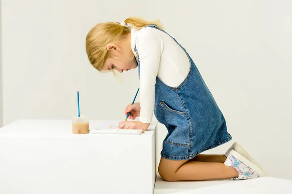 Cute Blonde Girl Sitting on Her Knees and Painting with Brush. — Stock Photo, Image