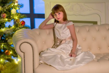 Yeni yıl ağacının yanındaki kanepede oturan güzel küçük kız..