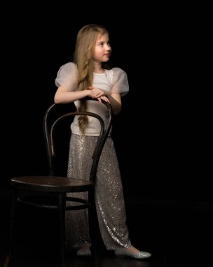 Eski Viyana sandalyesinin yanında siyah arka planda duran bir kızın portresi..