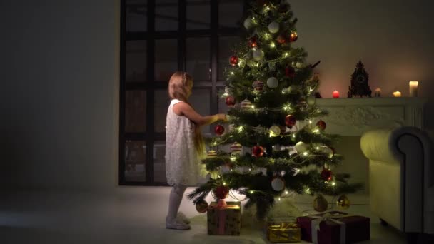 Klein meisje versiert een kerstboom. Nieuwjaarsconcept, gezinsvakanties. — Stockvideo