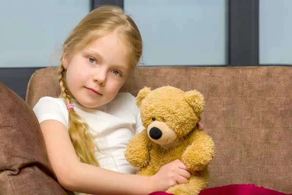 在沙发上抱着泰迪熊的小女孩. — 图库照片