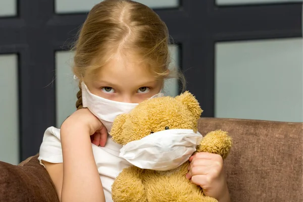 Egy kislány orvosi maszkban megölel egy plüssmacit. kovid fogalom. — Stock Fotó