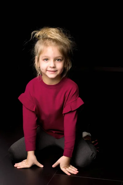 Χαμογελαστό ξανθό κορίτσι κάθεται στα γόνατά της ακουμπά τα χέρια στο στούντιο — Φωτογραφία Αρχείου
