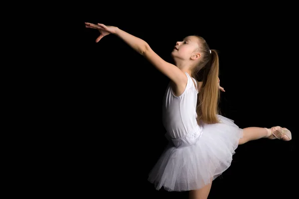 Cute little girl in a tutu and pointe shoes is dancing in the studio on a black background. — Stock Photo, Image
