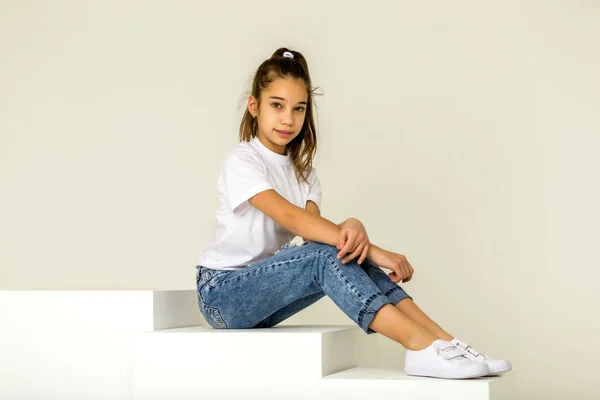 Το χαριτωμένο κοριτσάκι κάθεται στο στούντιο στις άσπρες σκάλες. στυλ και μόδα έννοια, ευτυχισμένη παιδική ηλικία. — Φωτογραφία Αρχείου