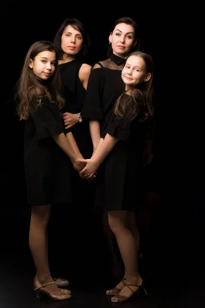 Jonge, mooie moeders met twee charmante dochters. Studio portret op een zwarte achtergrond. — Stockfoto